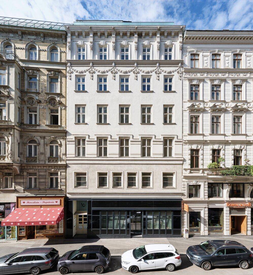 Klassisches Wiener Gebäude mit eleganter Fassade, vielen Fenstern und Geschäften im Erdgeschoss, an der Straße gelegen.