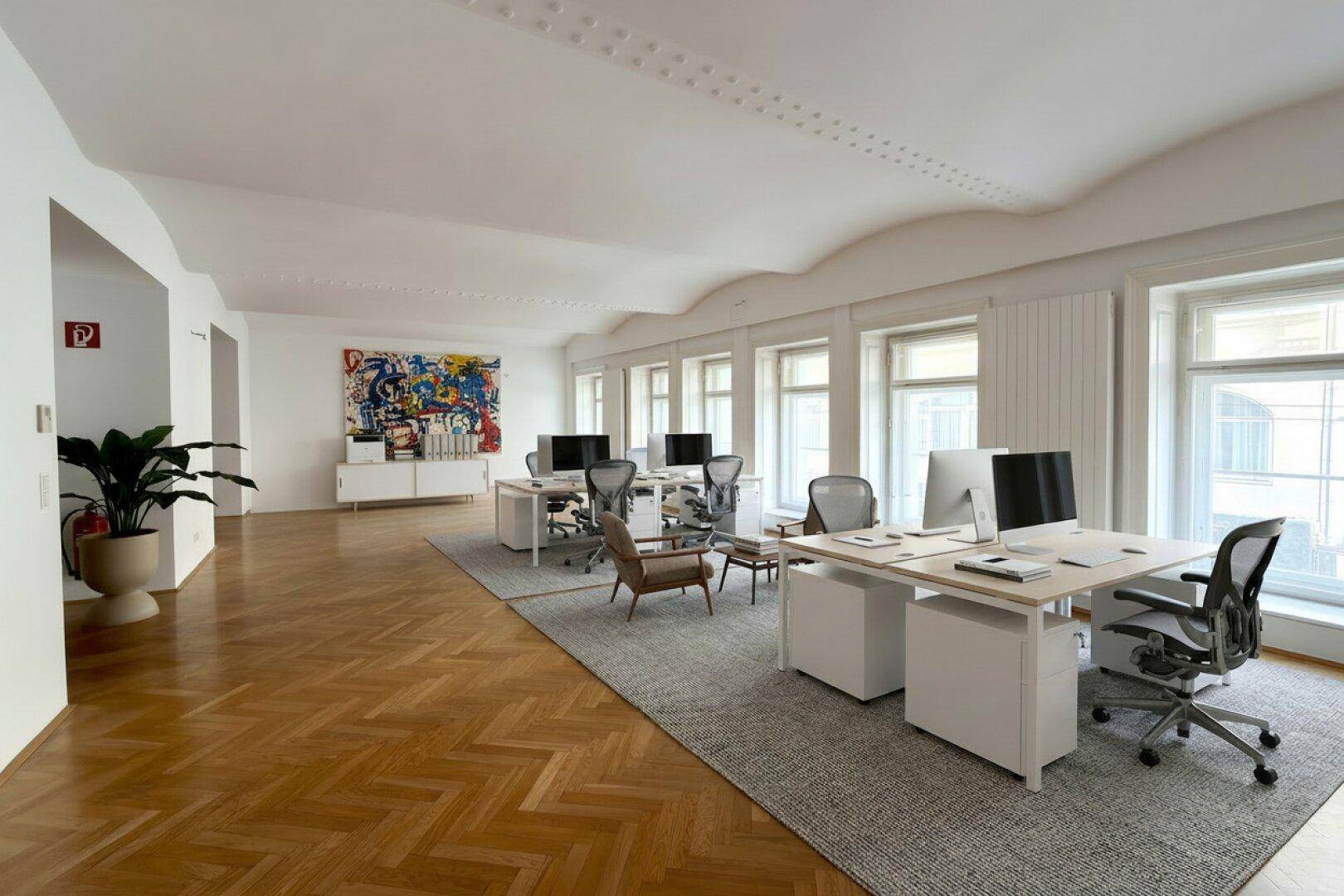 Großes Büro mit mehreren Arbeitsplätzen, Fischgrätparkett und einer markanten Deckenstruktur, sehr hell.