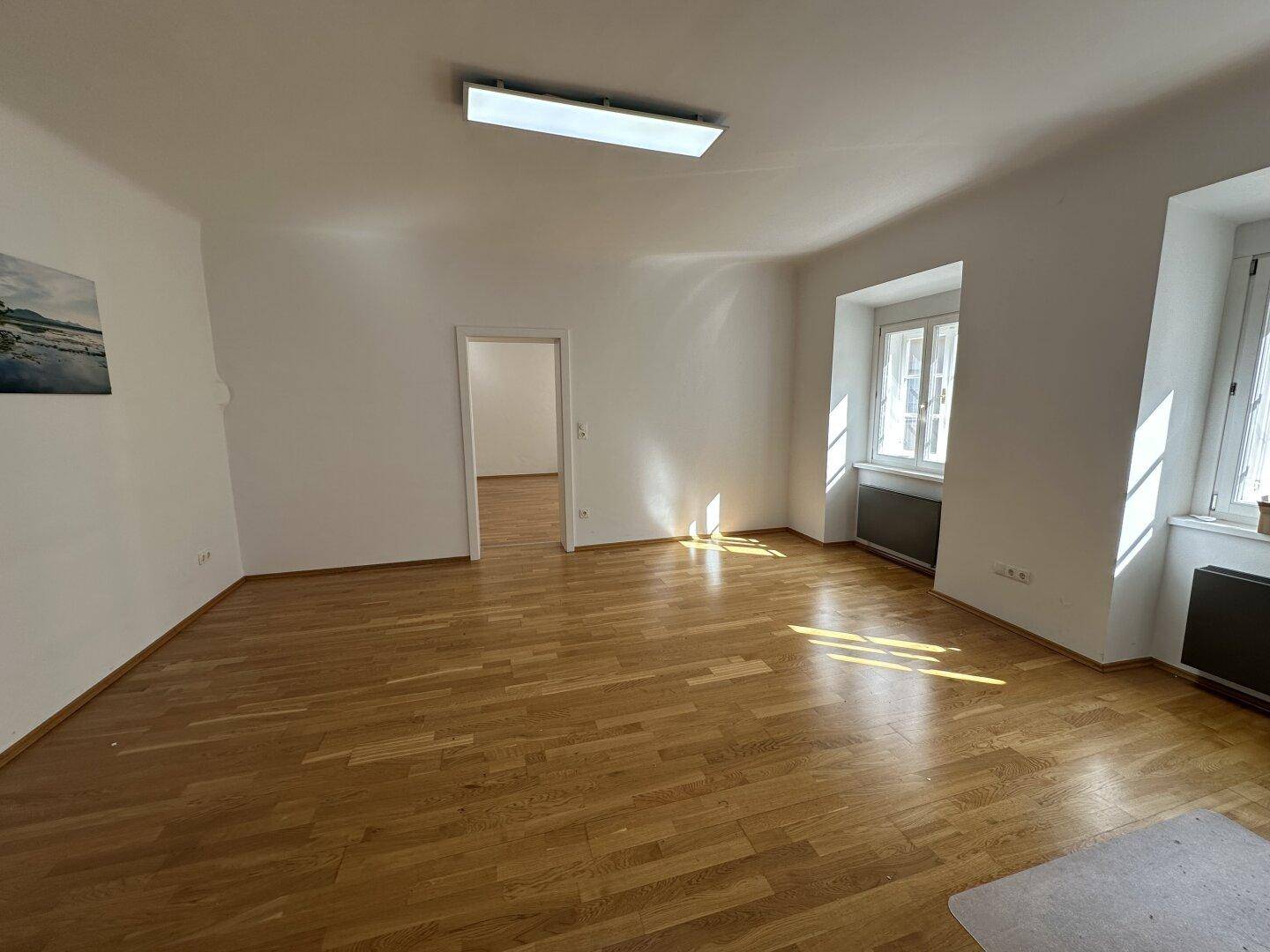 Geräumiges Wohnzimmer mit hellem Parkettboden, großen Fenstern und viel natürlichem Lichteinfall.