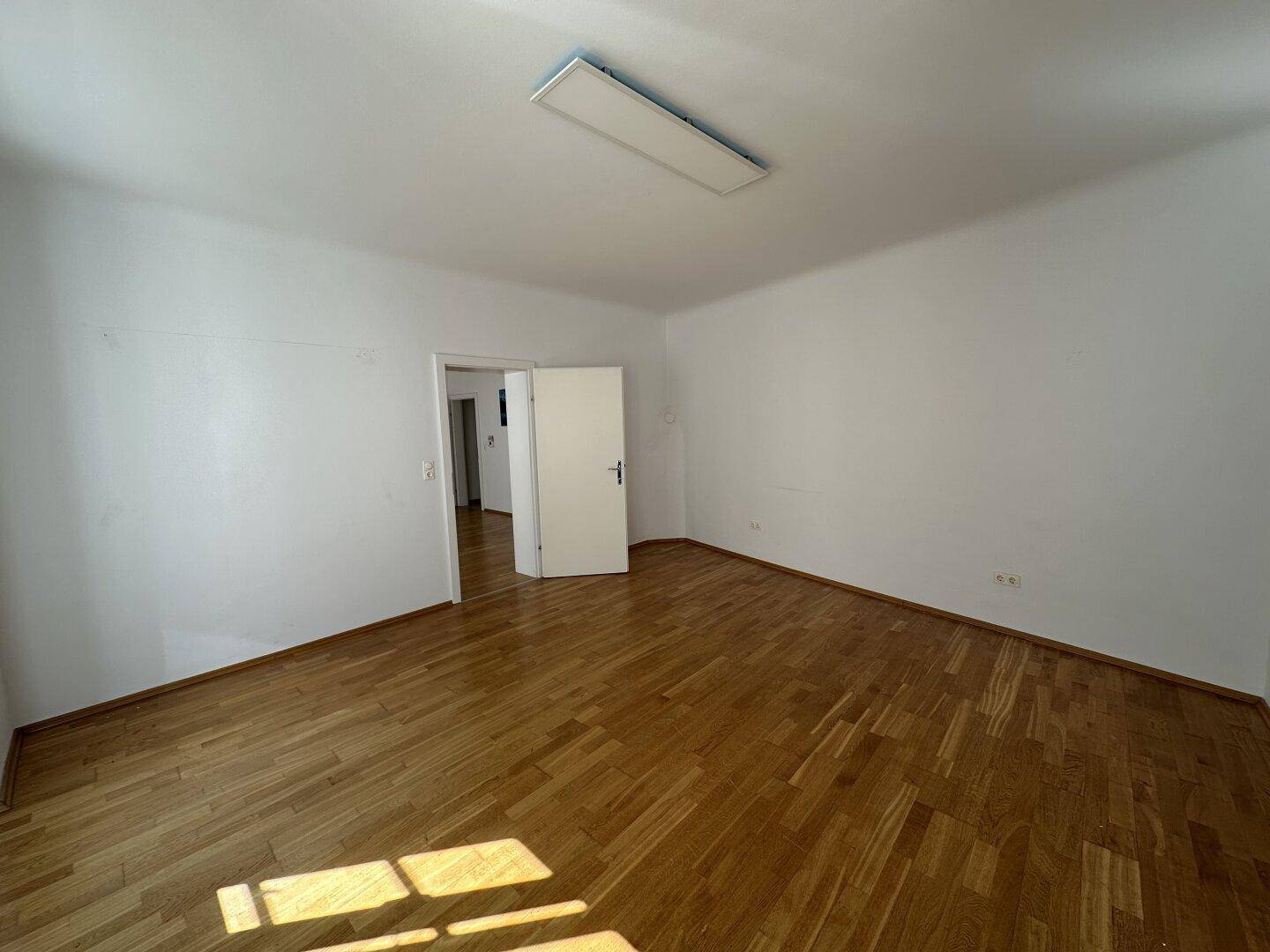 Helles Zimmer mit Parkettboden und weiß gestrichenen Wänden, ideal als Schlafzimmer oder Büro nutzbar.