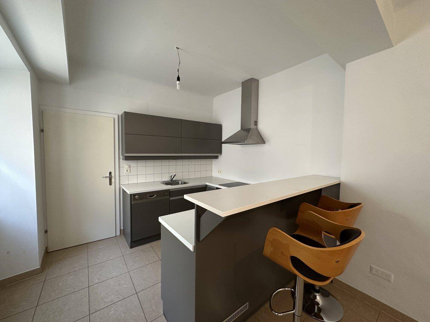 Moderne Küchenzeile mit grauen Schränken, weißer Arbeitsplatte und integrierter Frühstücksbar mit Hockern.