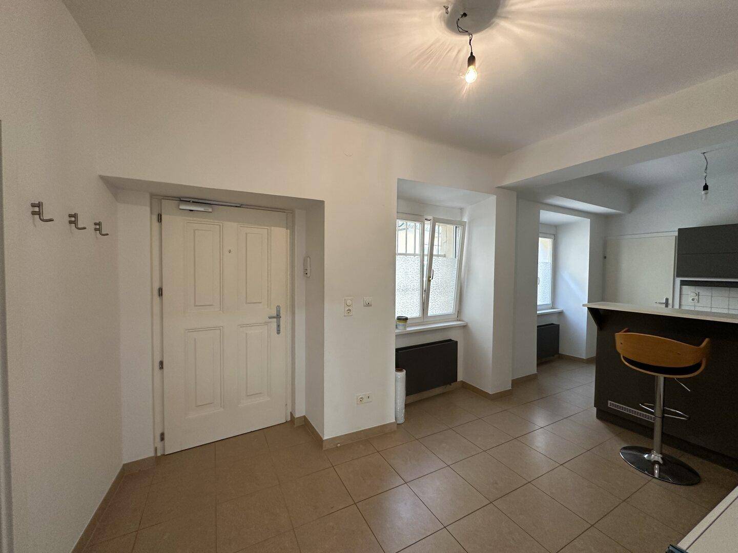 Heller Eingangsbereich mit Fliesenboden, Garderobenhaken und Blick auf eine moderne Küchenzeile mit Bar.