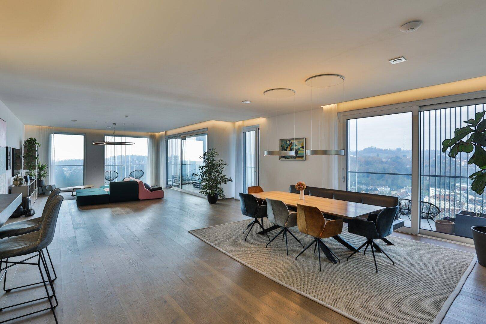 Weitläufiger Wohn- und Essbereich mit Panoramablick auf die Stadt durch raumhohe Fenster.