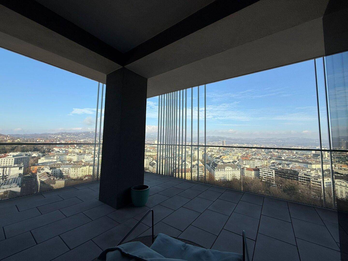 Geräumige Terrasse mit Glasbrüstung und weitem Blick über die Stadtlandschaft.