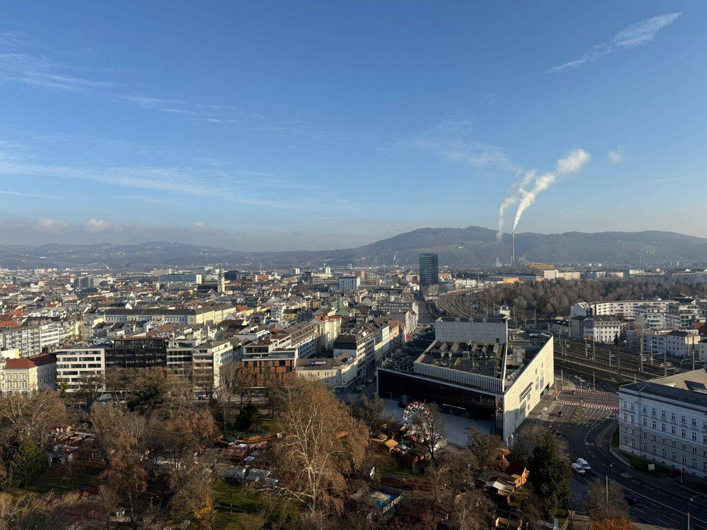 Weitläufiger Panoramablick über die Stadt mit Bergen im Hintergrund unter blauem Himmel.