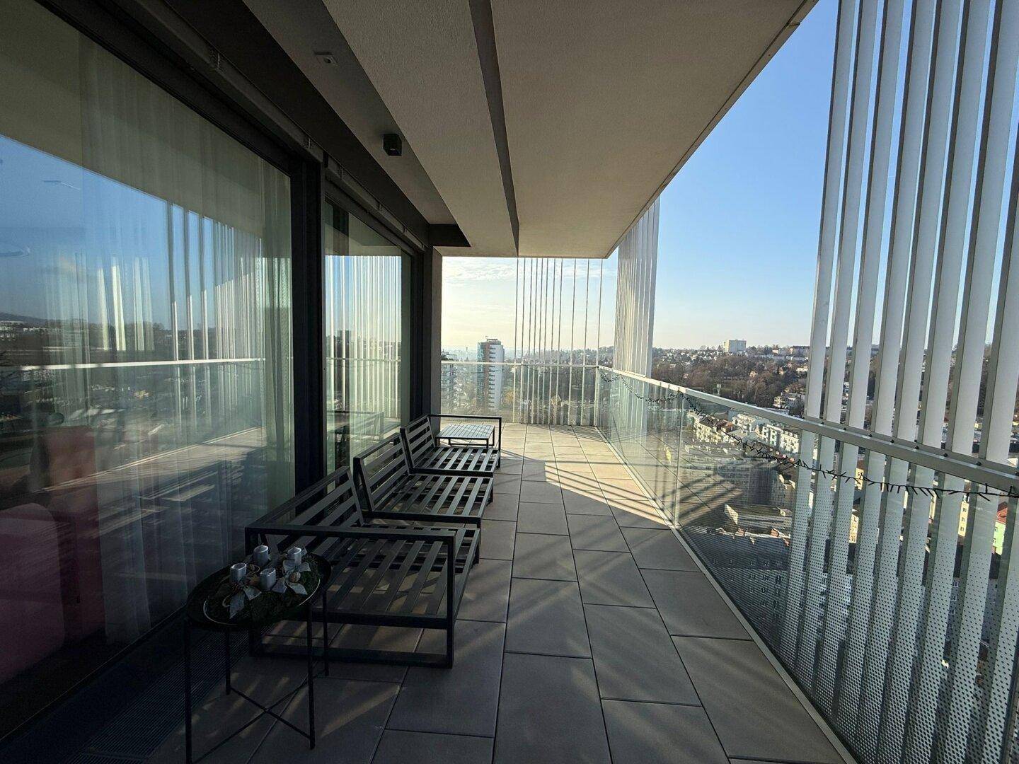 Heller Balkon mit Sitzgelegenheiten und sonnigem Ausblick auf die Stadt.