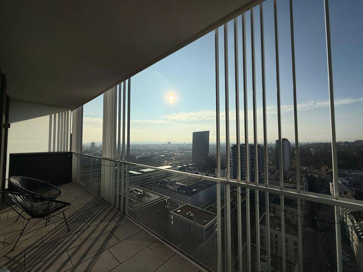 Sonniger Balkon mit minimalistischer Einrichtung und weitem Blick über die Stadt.