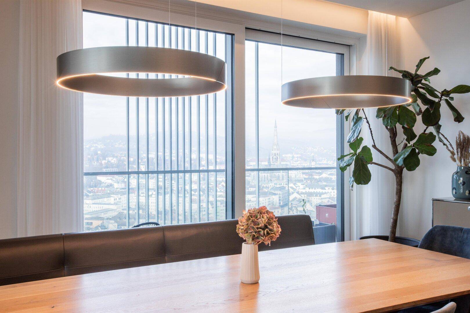 Esstisch mit modernem Design und beeindruckendem Stadtblick durch die großen Fenster.