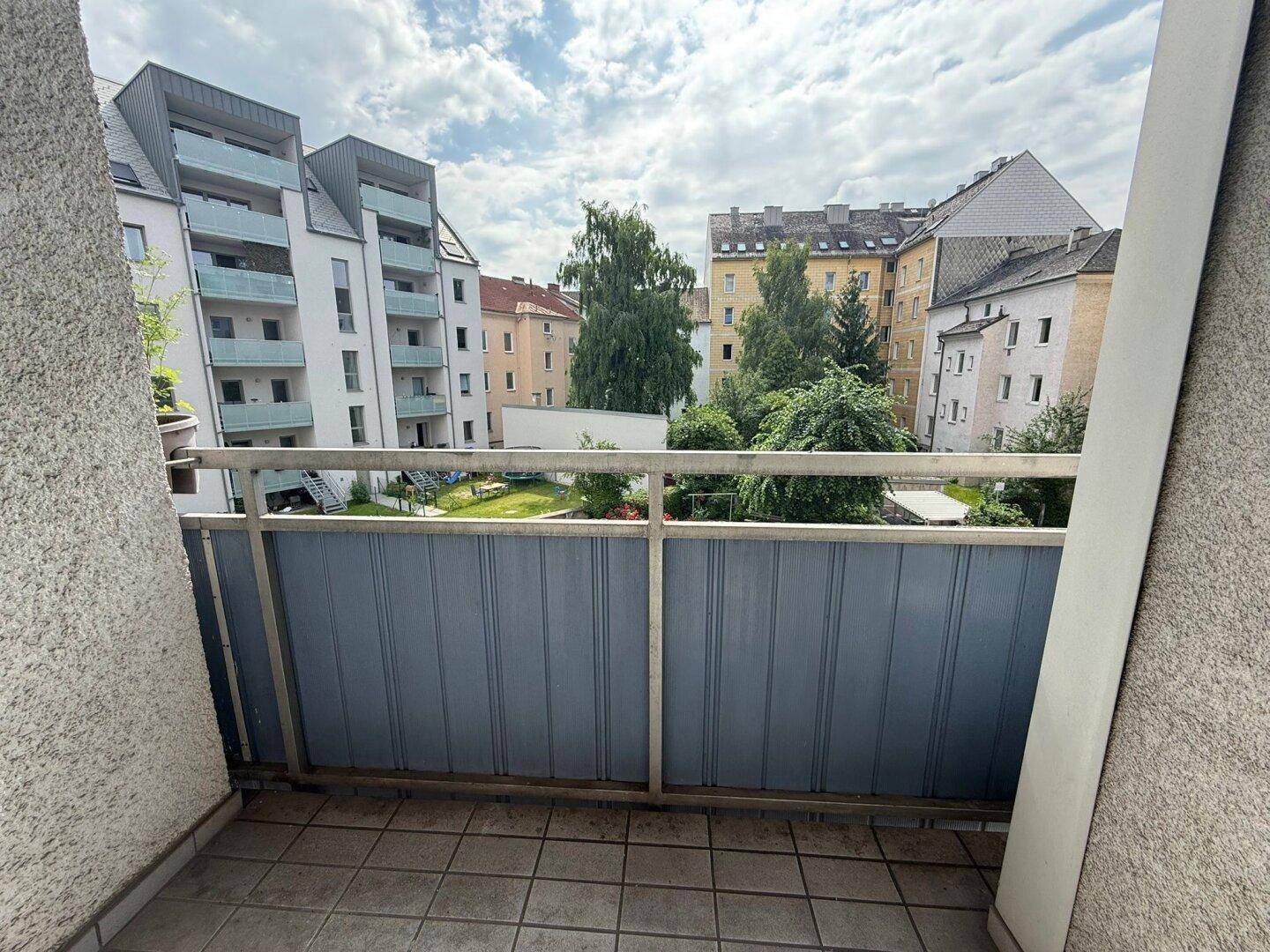 Balkon mit Blick auf den grünen Innenhof und die umliegenden Wohngebäude.