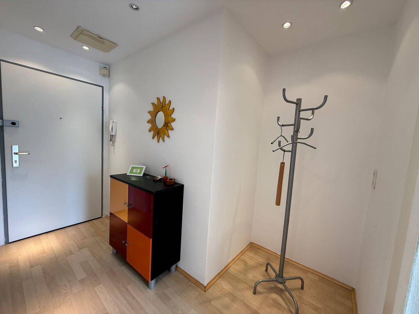 Heller Flur mit Eingangstür, farbigem Schrank und Garderobenständer.