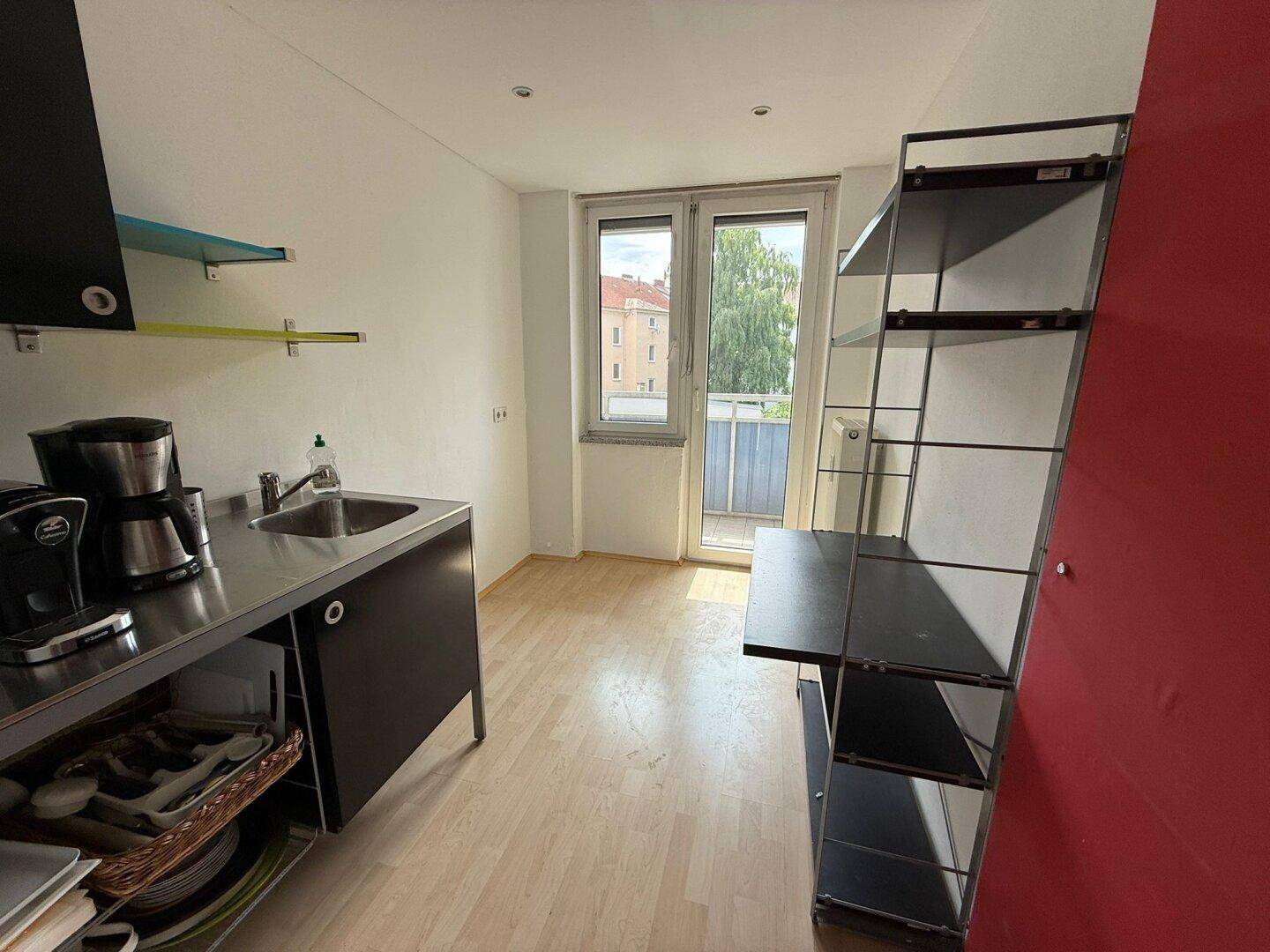 Küchenzeile mit Laminatboden, Fenster und Zugang zu einem kleinen Balkon.