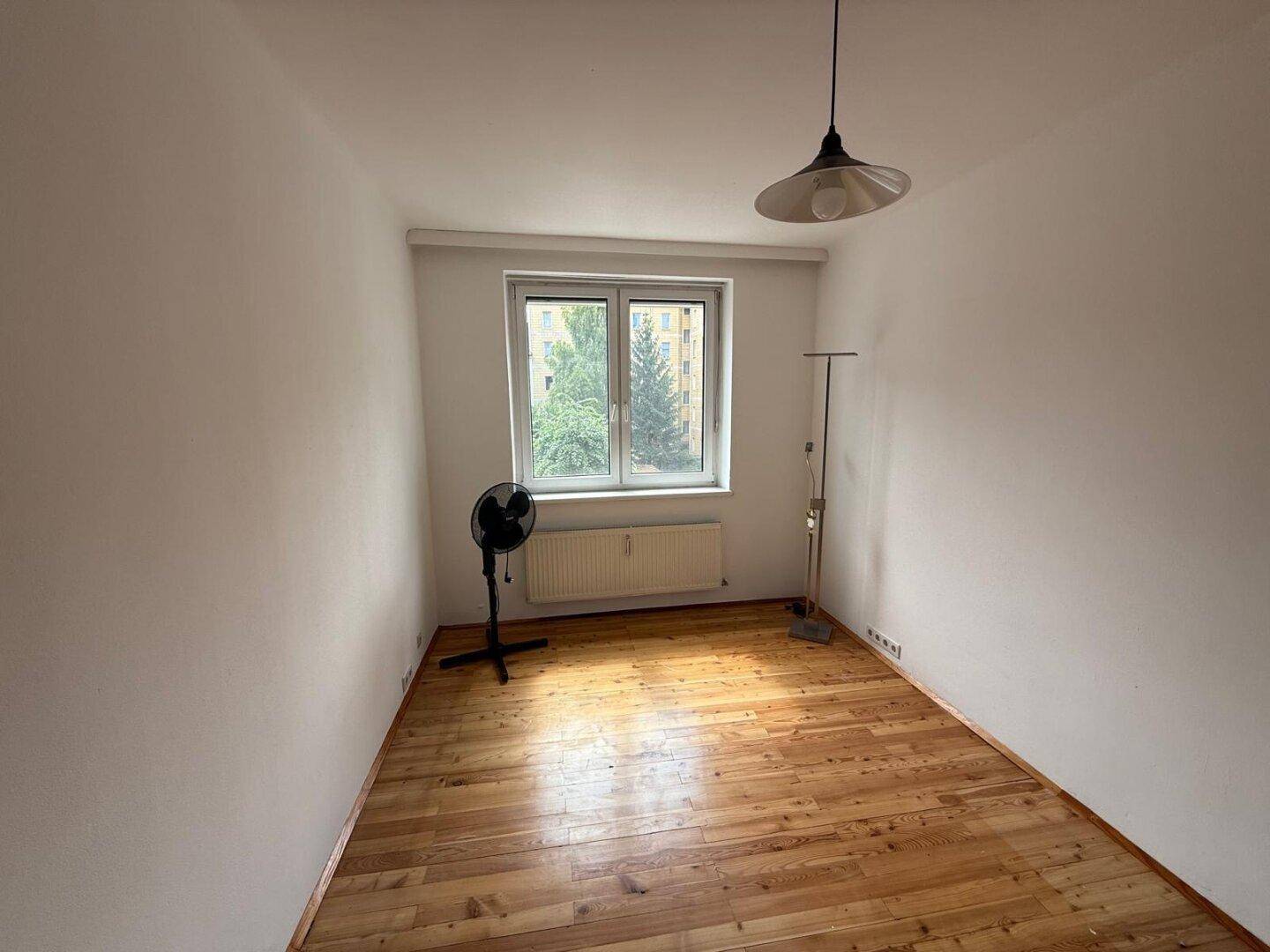 Helles Schlafzimmer mit Holzfußboden, großem Fenster und einem Ventilator.