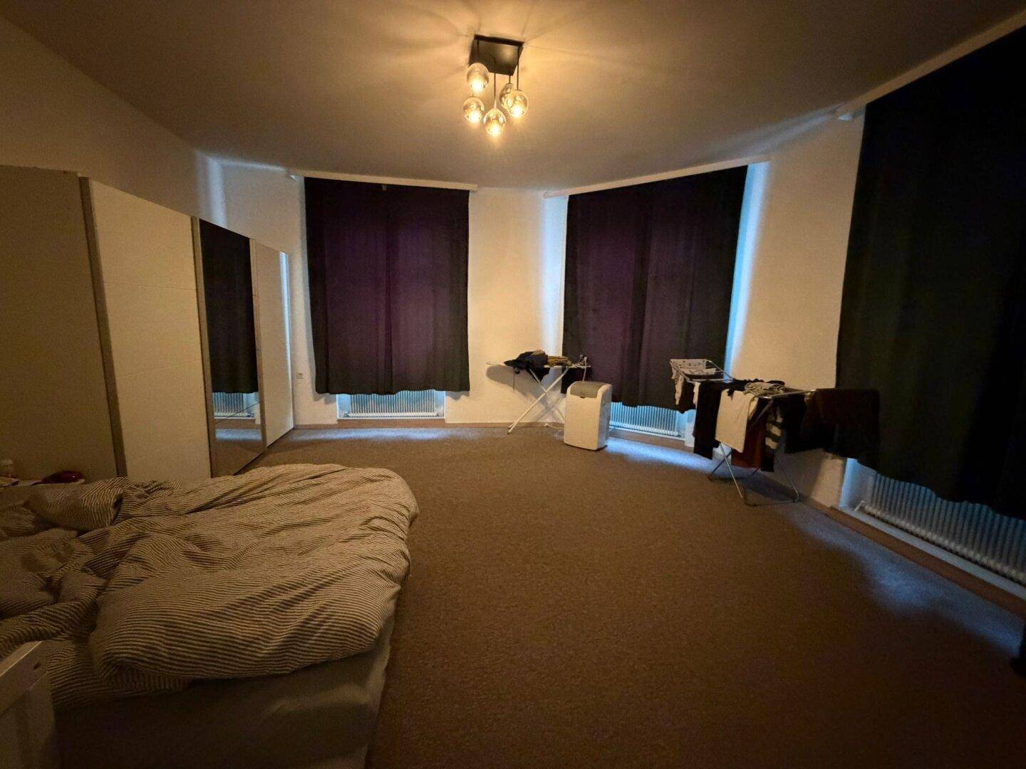 Schlafzimmer mit Teppichboden, dunklen Vorhängen und einem Bett in einem schlichten Stil.