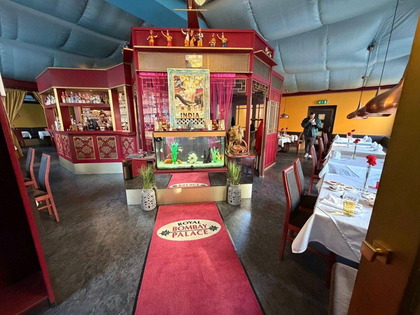 Innenansicht eines Restaurants mit indischer Dekoration, Tischen und einem Aquarium.