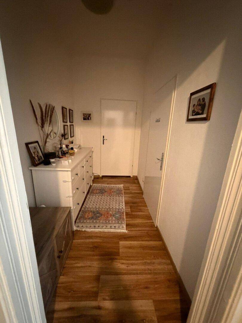 Heller Flur mit Holzfußboden, einer Kommode und einem Spiegel an der Wand.