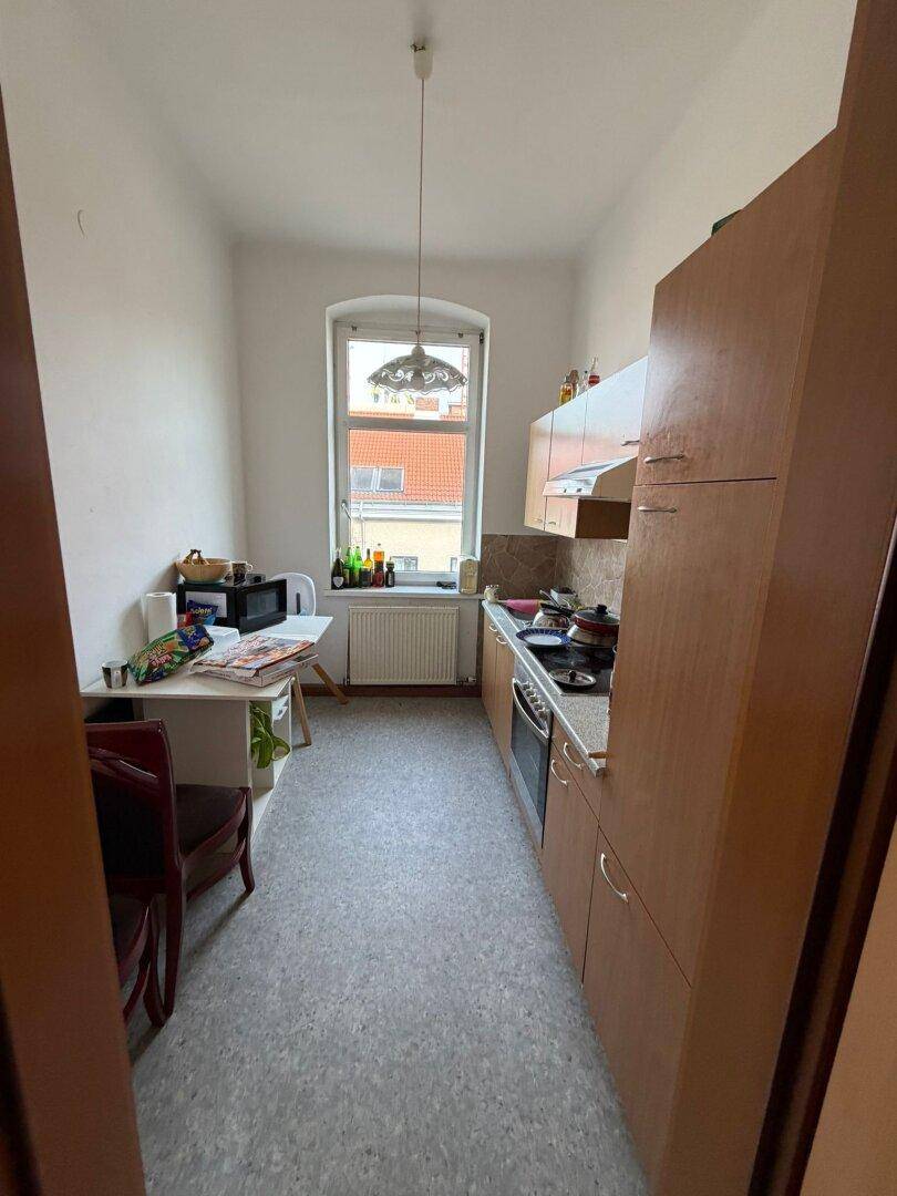 Kleine Küche mit Linoleumboden, Holzschränken und einem Fenster mit Blick nach draußen.
