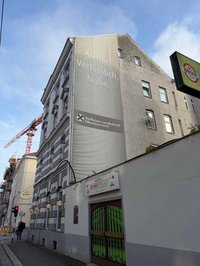 Seitenansicht eines Gebäudes mit großer Werbeplane und einem Kran im Hintergrund.