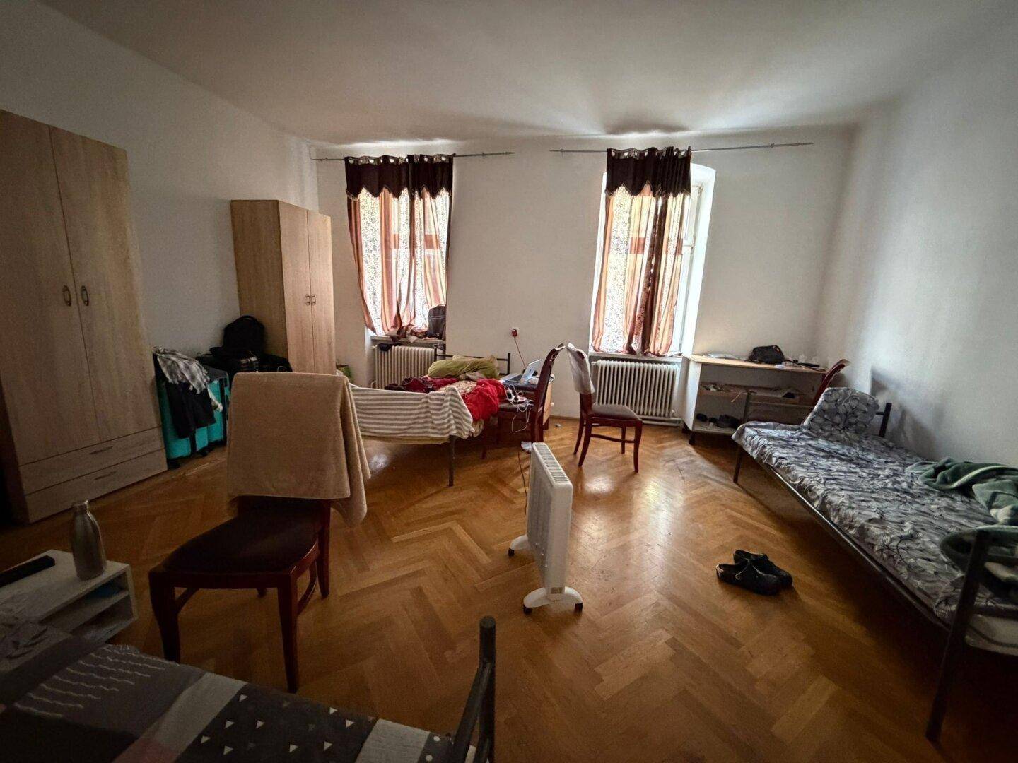 Geräumiges Schlafzimmer mit Fischgrätparkett, mehreren Betten und einem Heizkörper.