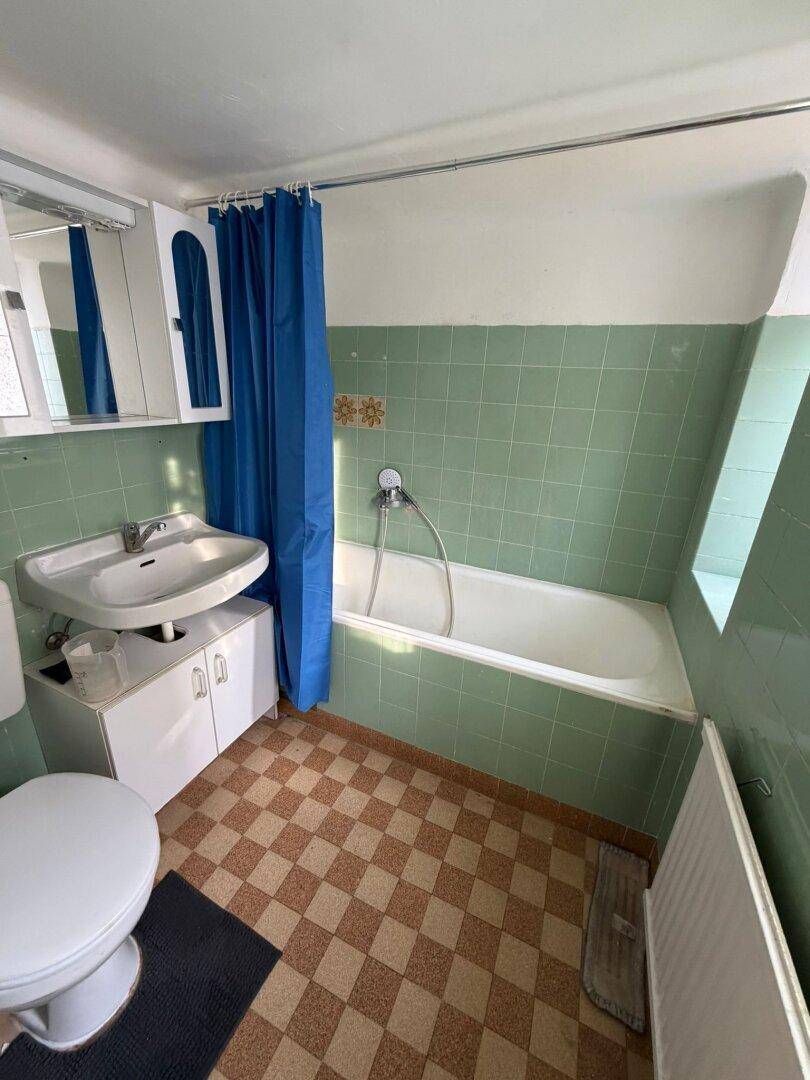 Badezimmer mit grünen Wandfliesen, Badewanne und einem karierten Linoleumboden.