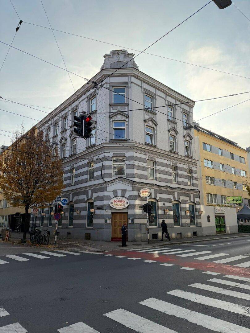 Eckgebäude mit traditioneller Architektur und Geschäften im Erdgeschoss an einer städtischen Kreuzung.