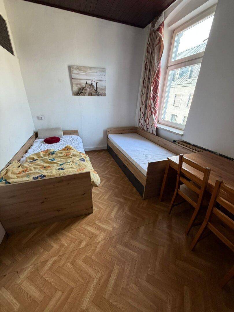 Schlafzimmer mit Holzfußboden, zwei Einzelbetten und einem Schreibtisch am Fenster.