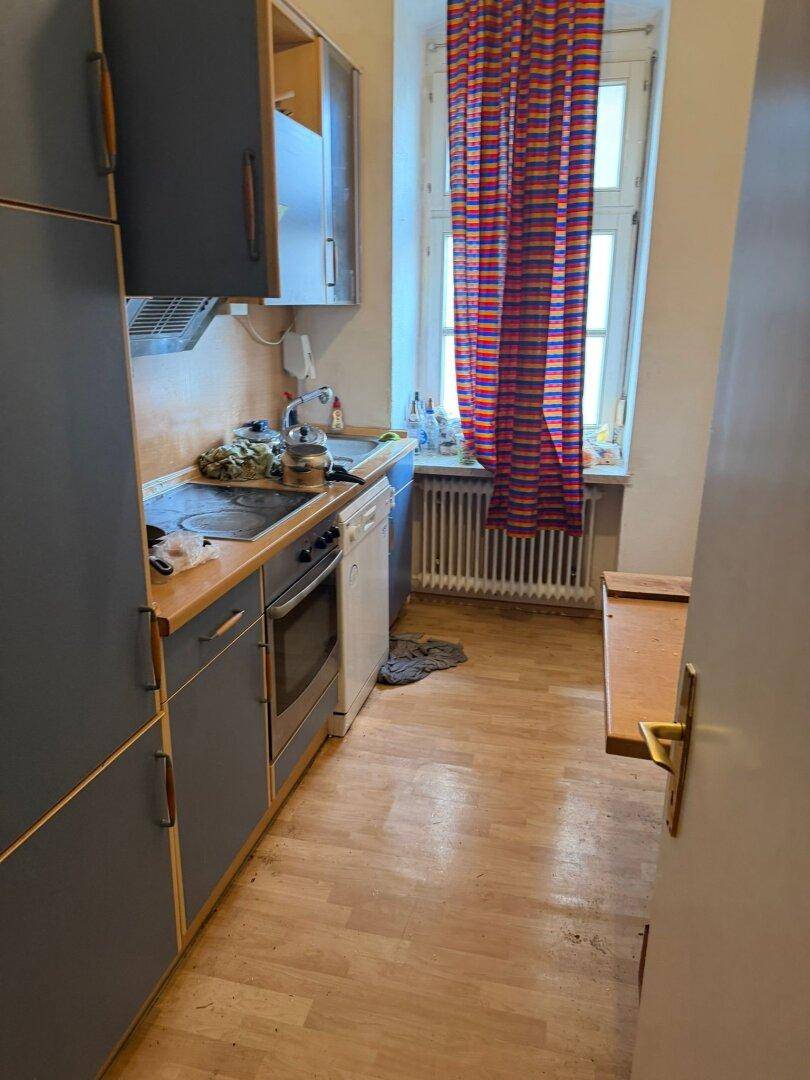 Schmale Küche mit Holzfußboden, blauen Schränken und einem Fenster über der Spüle.