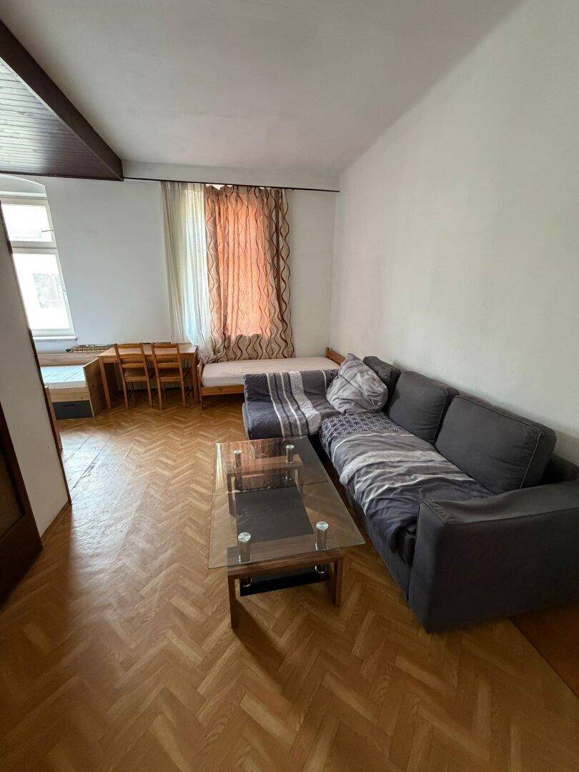 Wohnzimmer mit Fischgrätparkett, einem Sofa und einem Couchtisch aus Glas.