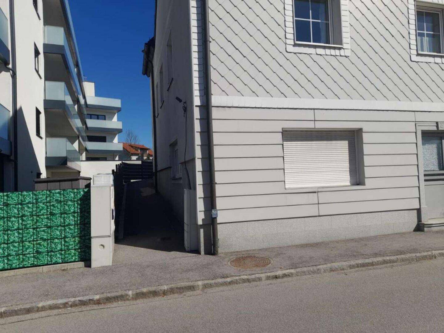 Seitenansicht des Gebäudes mit einem Durchgang und einem grünen Zaun.