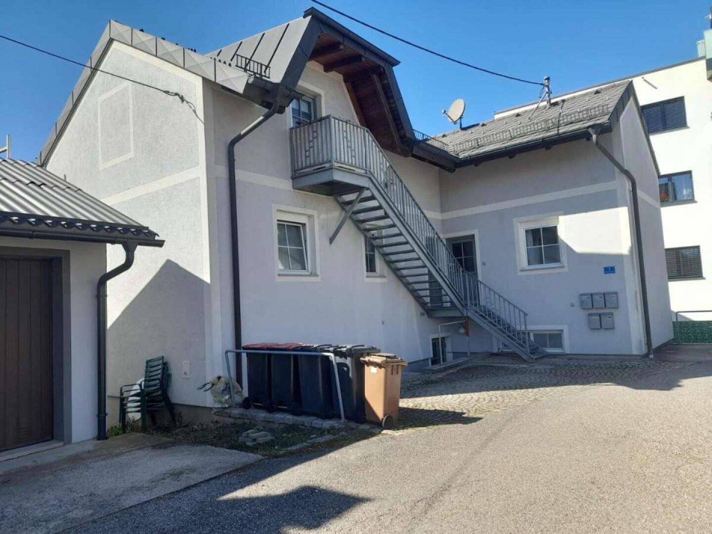 Rückseite des Gebäudes mit Außentreppe und Mülltonnen auf dem Hof.