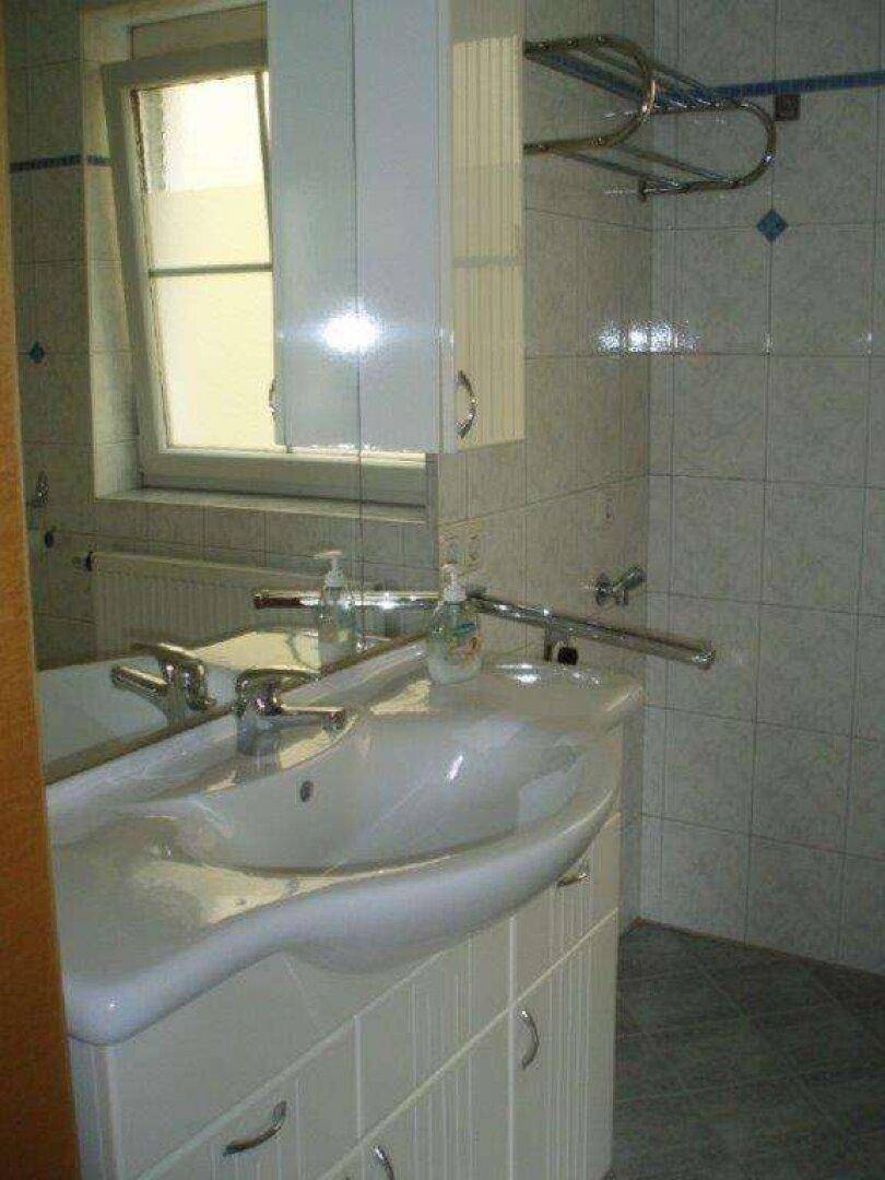 Badezimmer mit Doppelwaschbecken, Spiegelschrank und Fenster für Tageslicht.