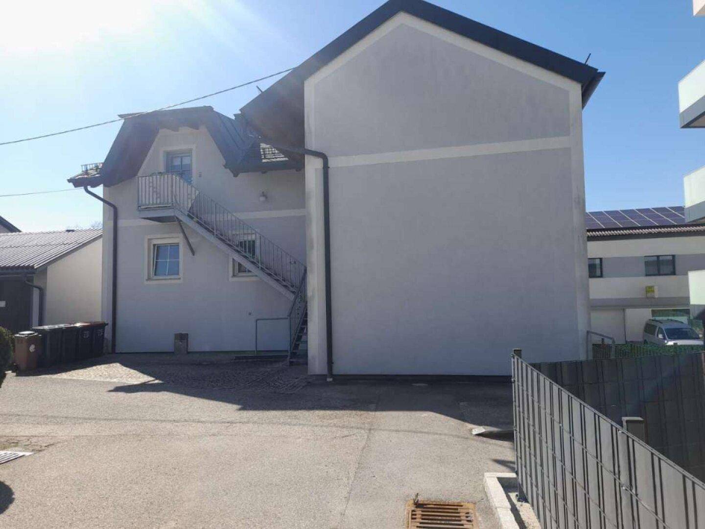 Rückansicht des Hauses mit Außentreppe und sonnigem Hofbereich.