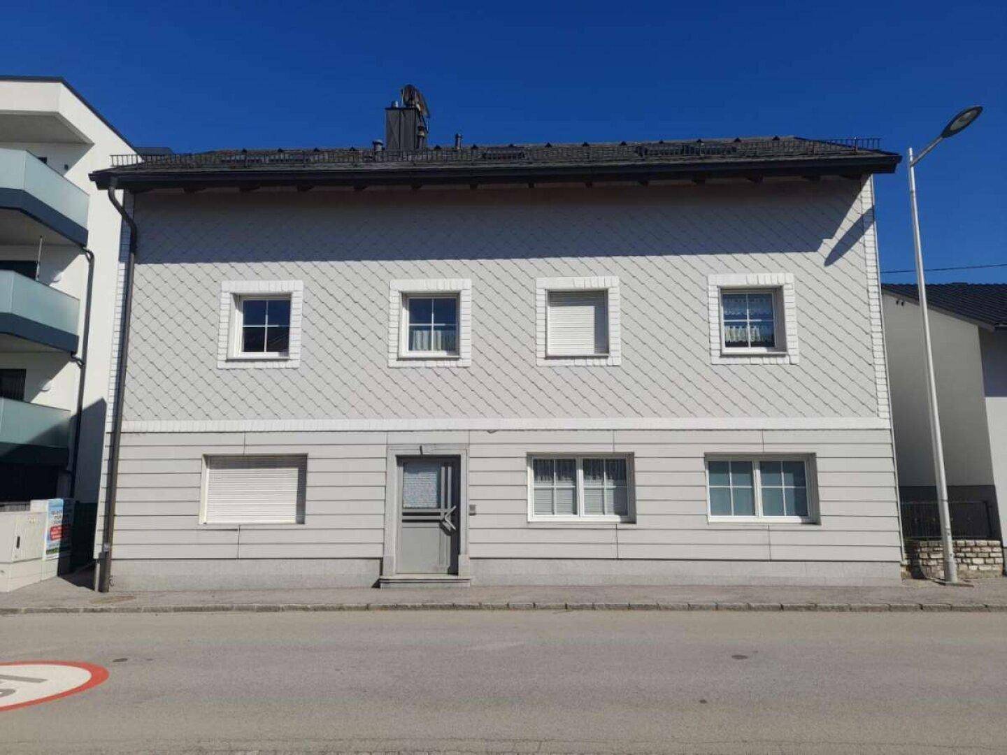 Vorderansicht des Hauses mit grauer Fassade, Schindeln und Rollläden.