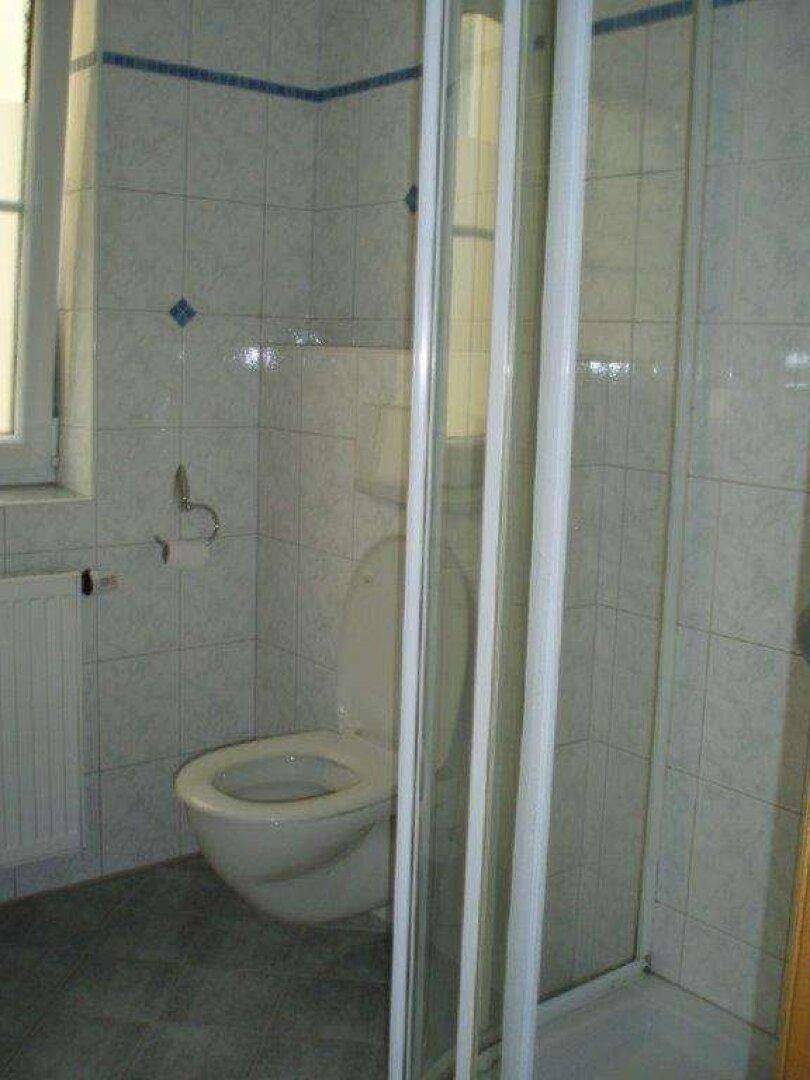 Badezimmer mit Duschkabine, Toilette und Fenster, vollständig gefliest.