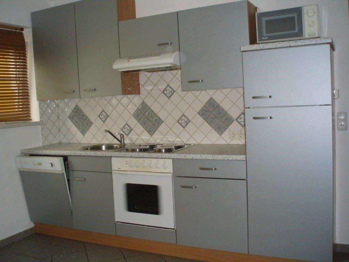 Graue Küche mit integrierten Geräten, Kühlschrank und Mikrowelle.