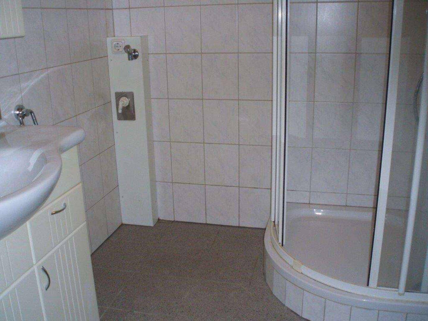 Helles Badezimmer mit Duschkabine, Waschbecken und weißen Fliesen.