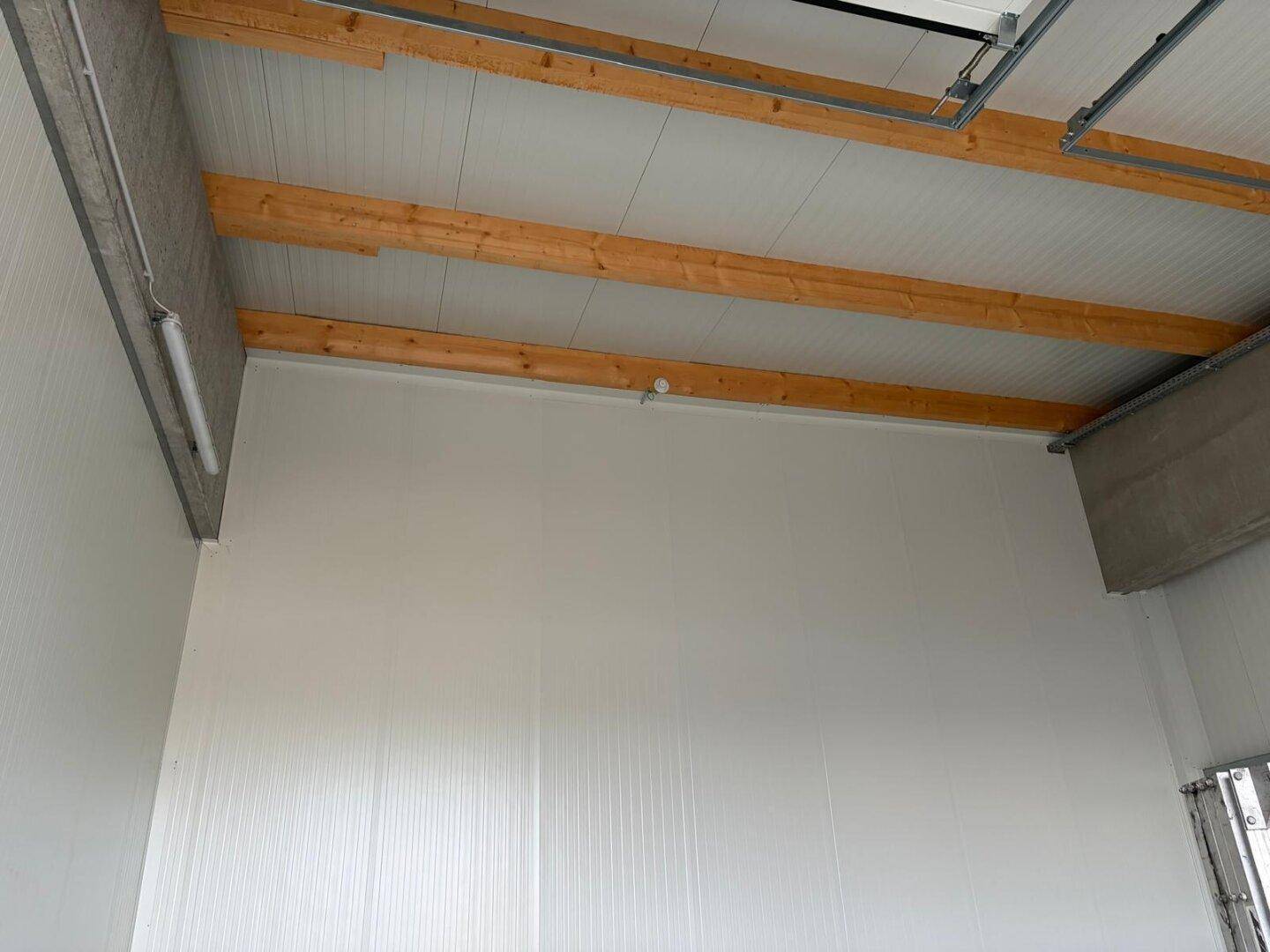 Hoher Innenraum einer Lagerhalle mit weißen Wänden und sichtbaren Holzdeckenbalken.