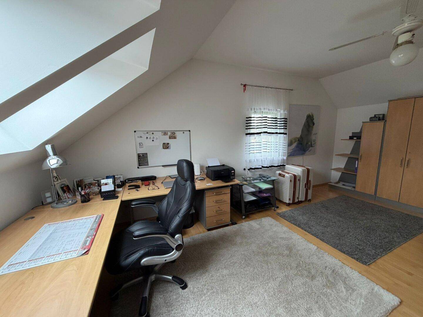 Helles Arbeitszimmer mit Dachschrägen, Holzmöbeln und Teppichboden.