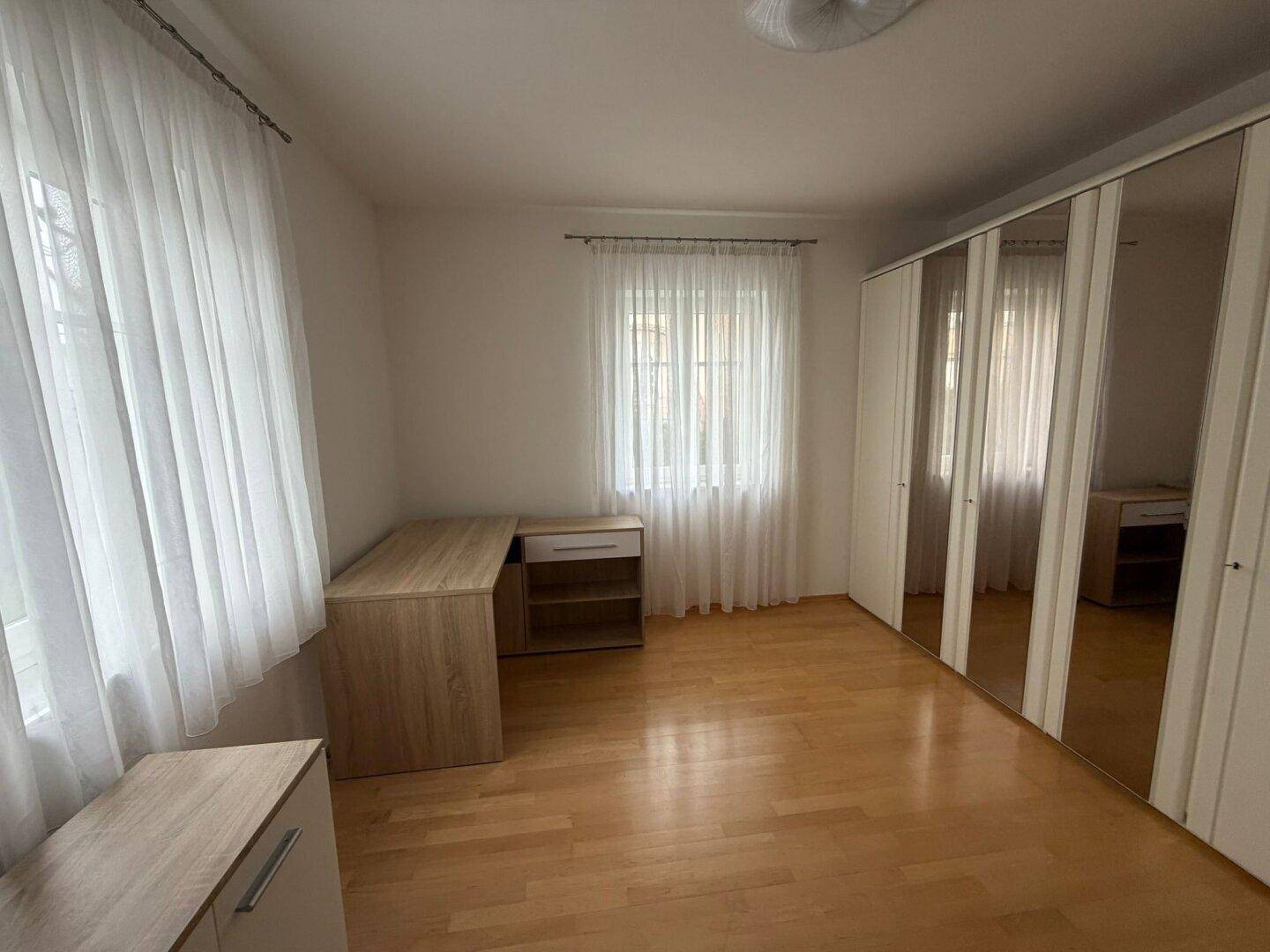 Helles Schlafzimmer mit Holzfußboden, Spiegelschränken und Schreibtisch.