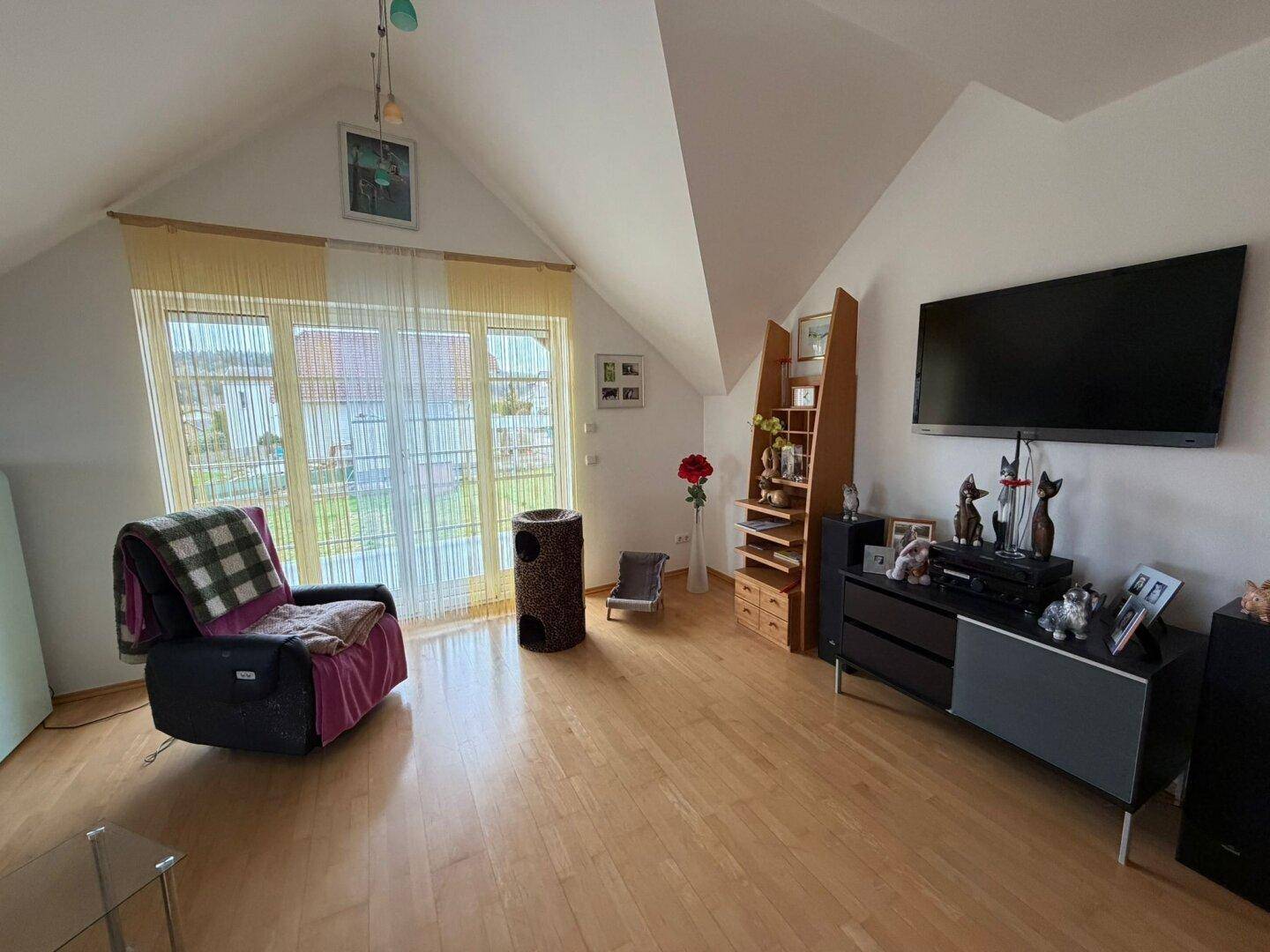 Helles Wohnzimmer im Dachgeschoss mit Dachschrägen, Holzfußboden und großem Fenster.