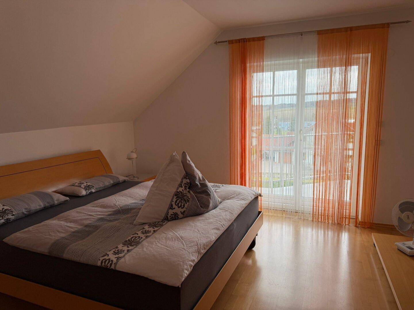 Helles Schlafzimmer mit Doppelbett, Holzfußboden und Zugang zum Balkon.