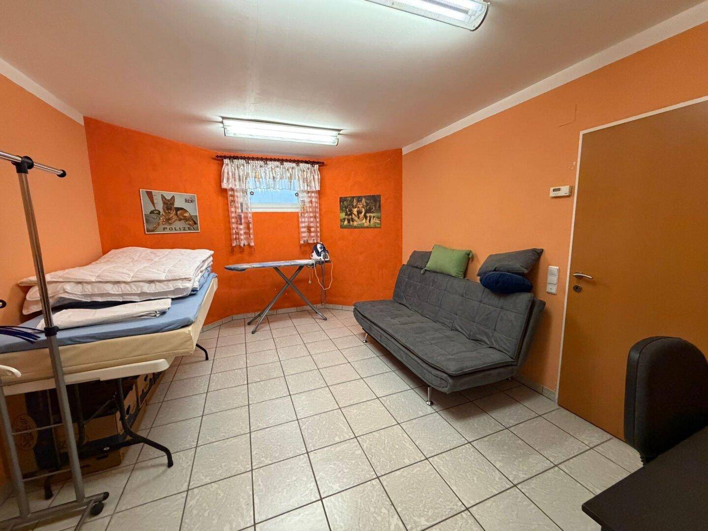 Vielseitiger Raum mit orangefarbenen Wänden, Fliesenboden und Schlafsofa.