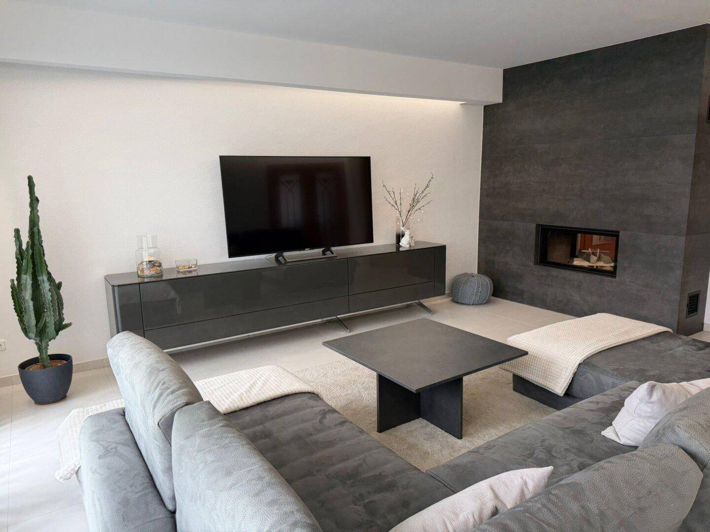 Helles Wohnzimmer mit modernem Kamin, großem Fernseher und bequemer Sitzecke.