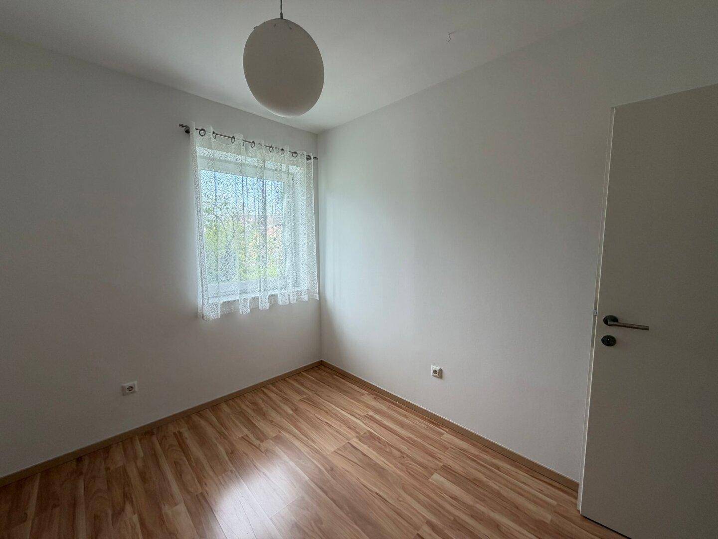 Helles, leeres Zimmer mit Laminatboden und einem Fenster, ideal als Schlafzimmer.