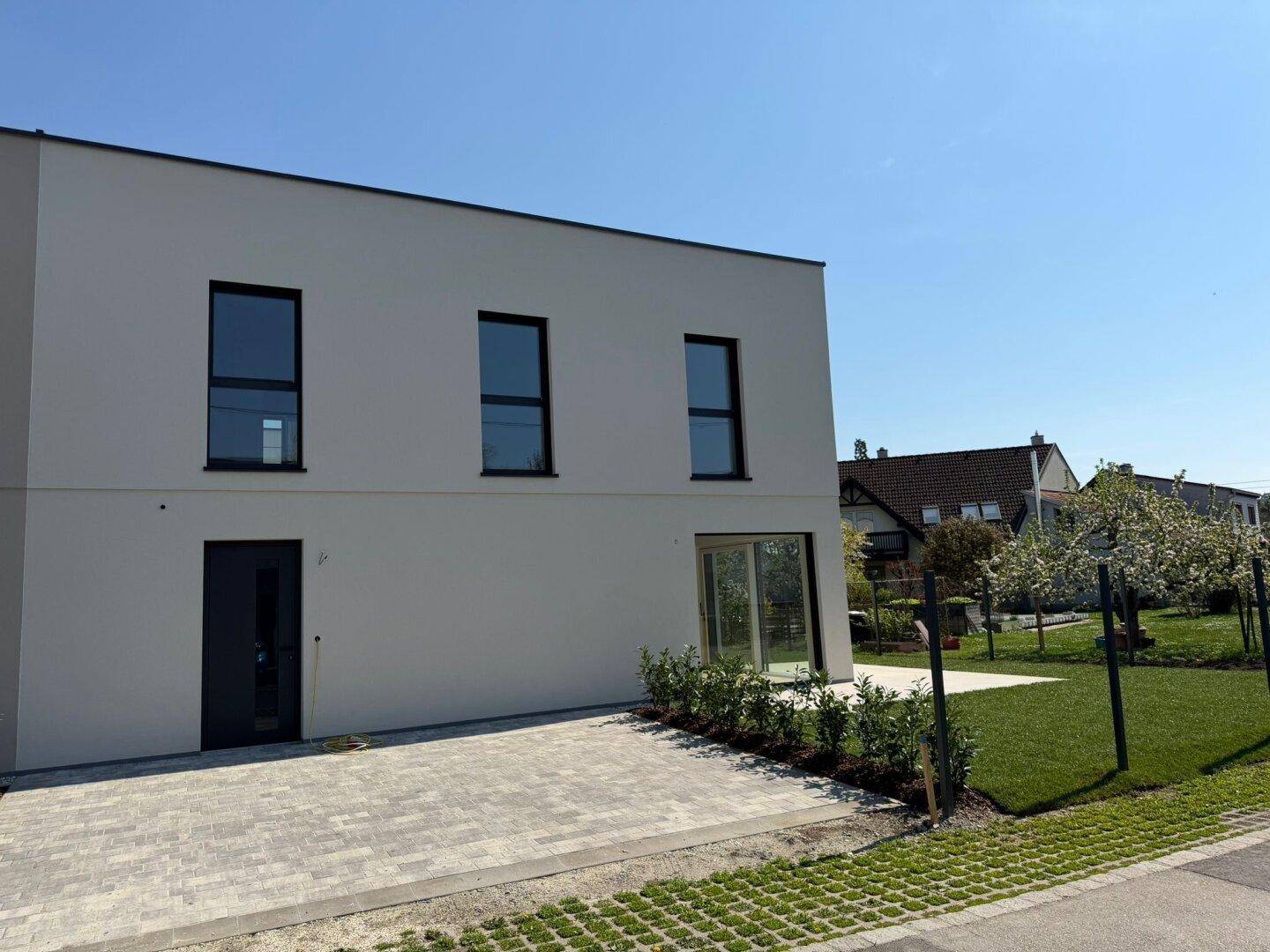 Seitenansicht des modernen Neubaus mit gepflasterter Zufahrt und großen Fenstern.