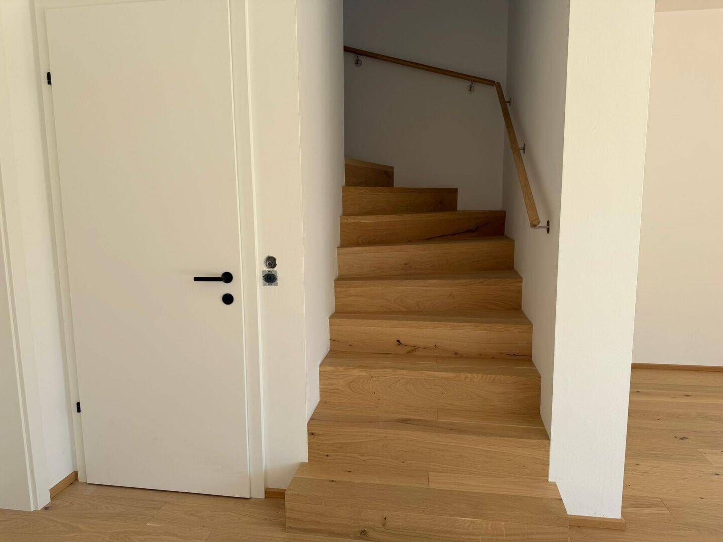 Moderne Holztreppe mit hellem Geländer, die die verschiedenen Etagen des Hauses verbindet.