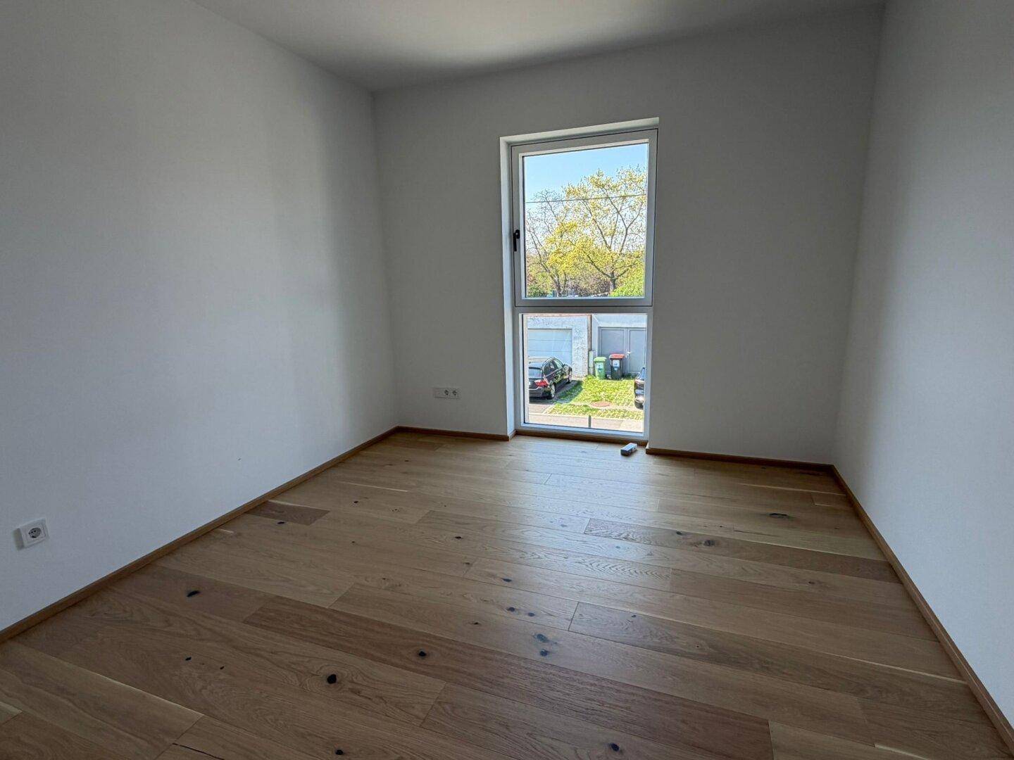 Helles Schlafzimmer mit Eichenparkettboden und großem Fenster mit Blick ins Grüne.