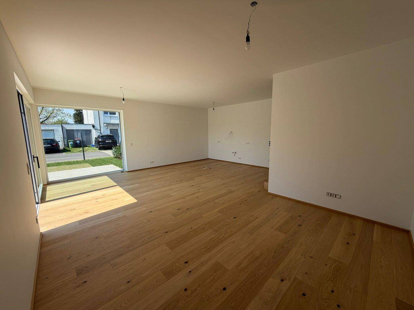 Geräumiges Wohnzimmer mit hellem Eichenparkett und großen Fenstern zur Vorderseite des Hauses.