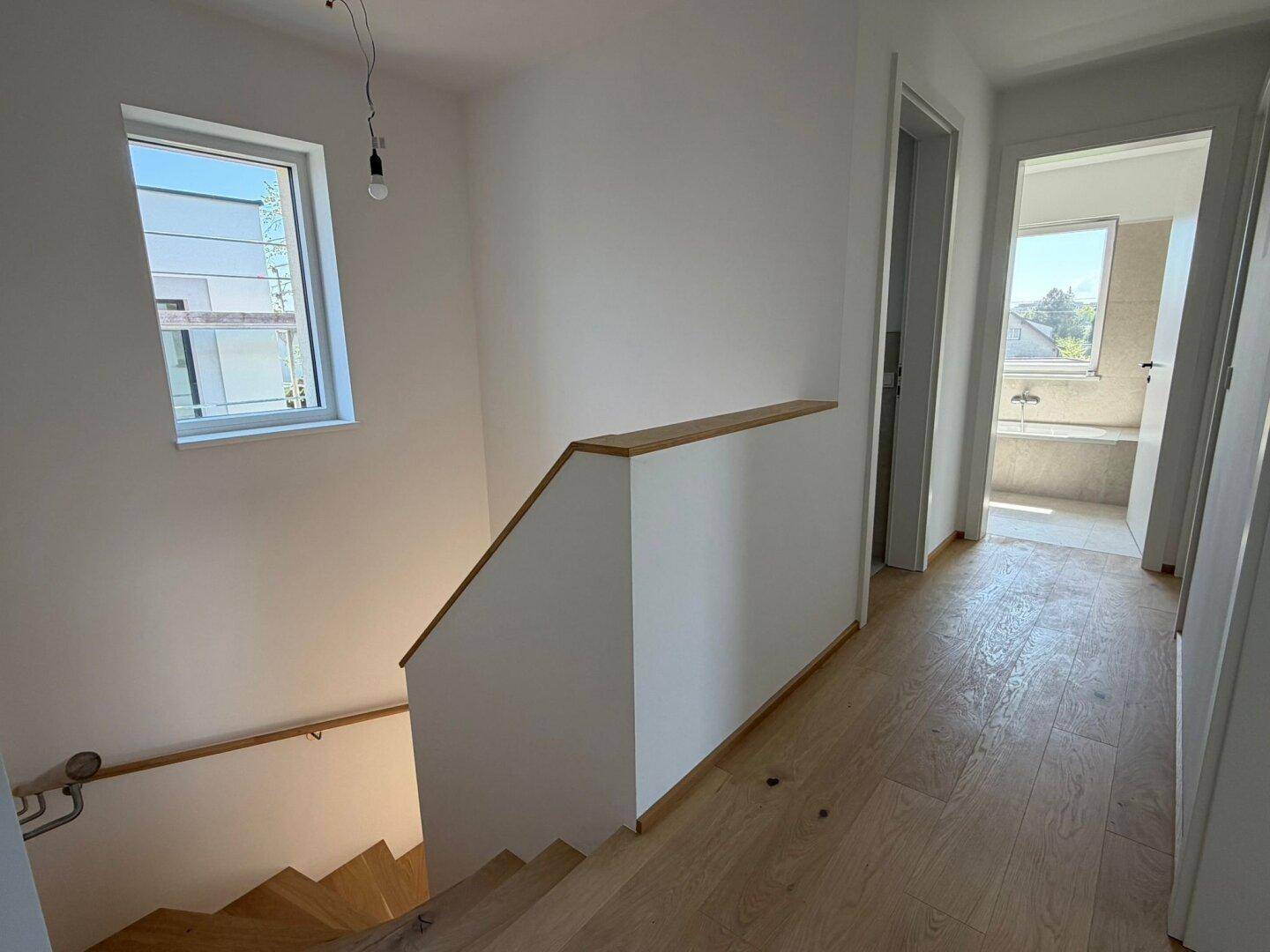 Heller Flur im Obergeschoss mit Holzgeländer und Blick in das moderne Badezimmer.