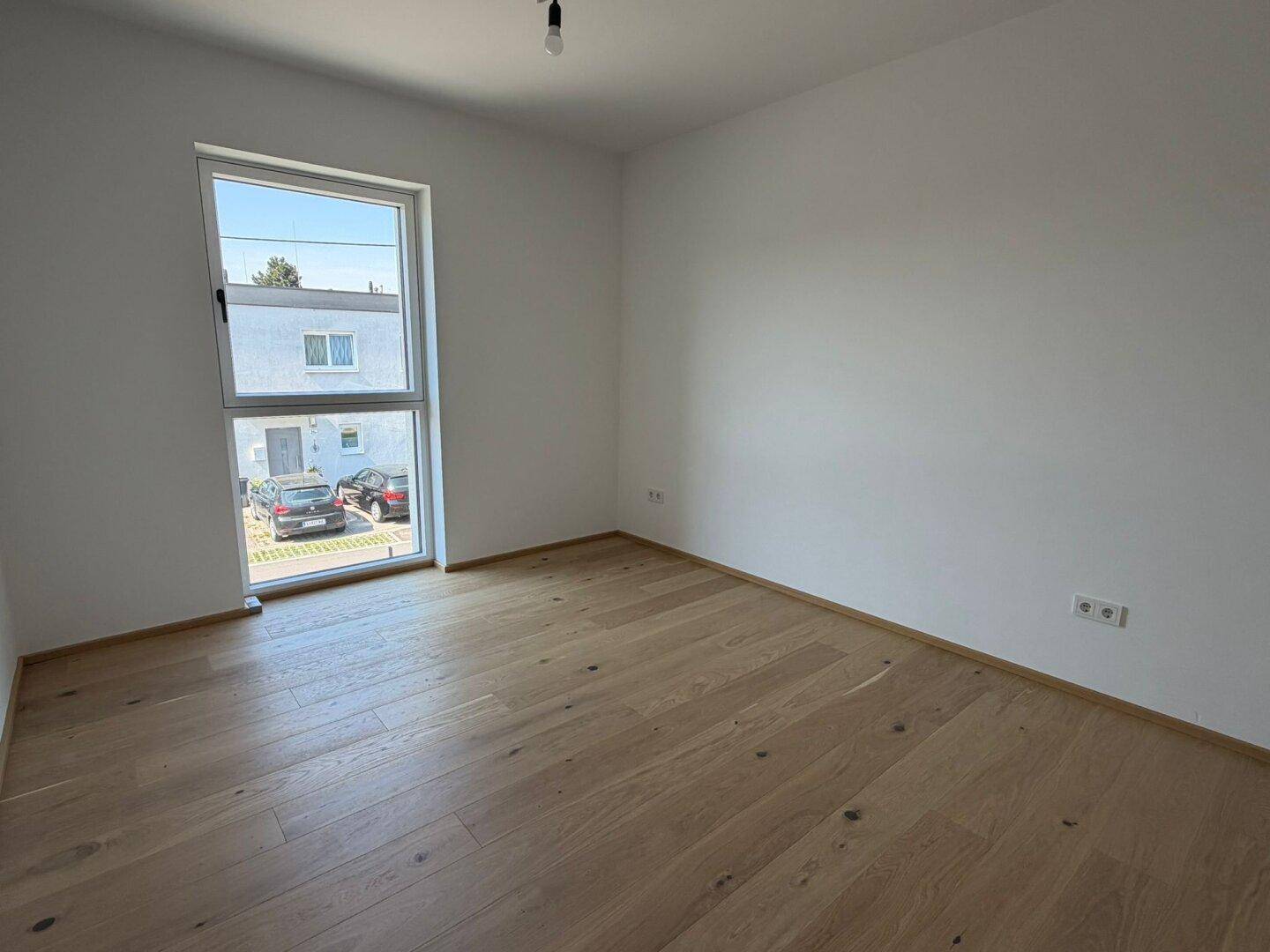 Geräumiges Schlafzimmer mit hellem Eichenparkett und großem Fenster zur Straßenseite.
