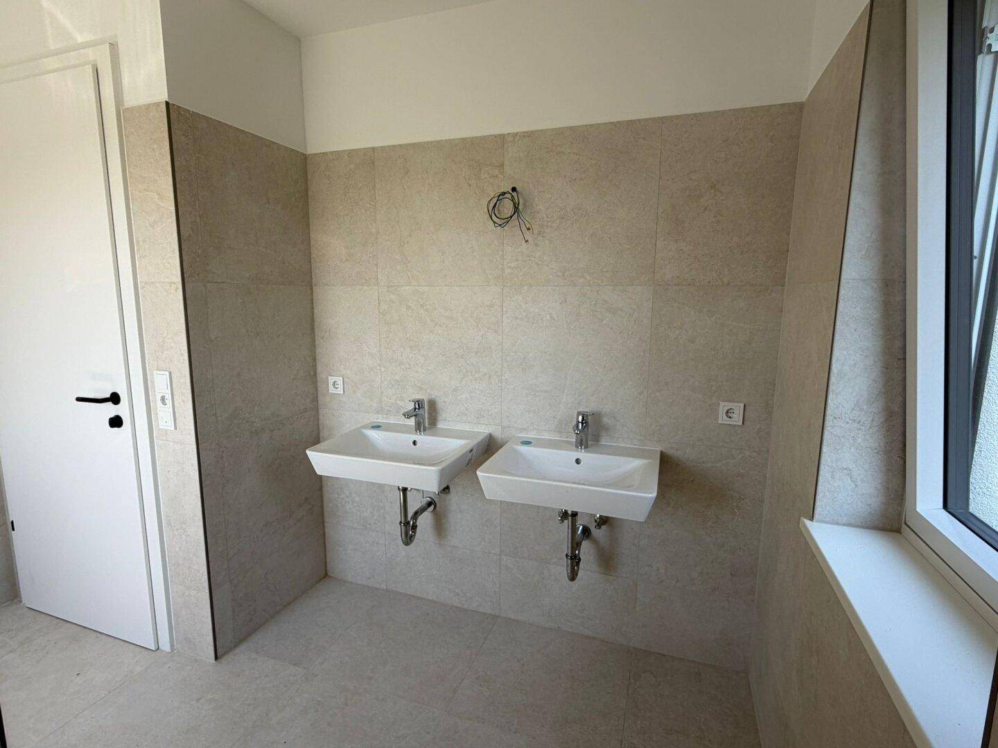 Helles Badezimmer mit zwei Waschbecken und modernen Fliesen, bereit für die Endmontage.